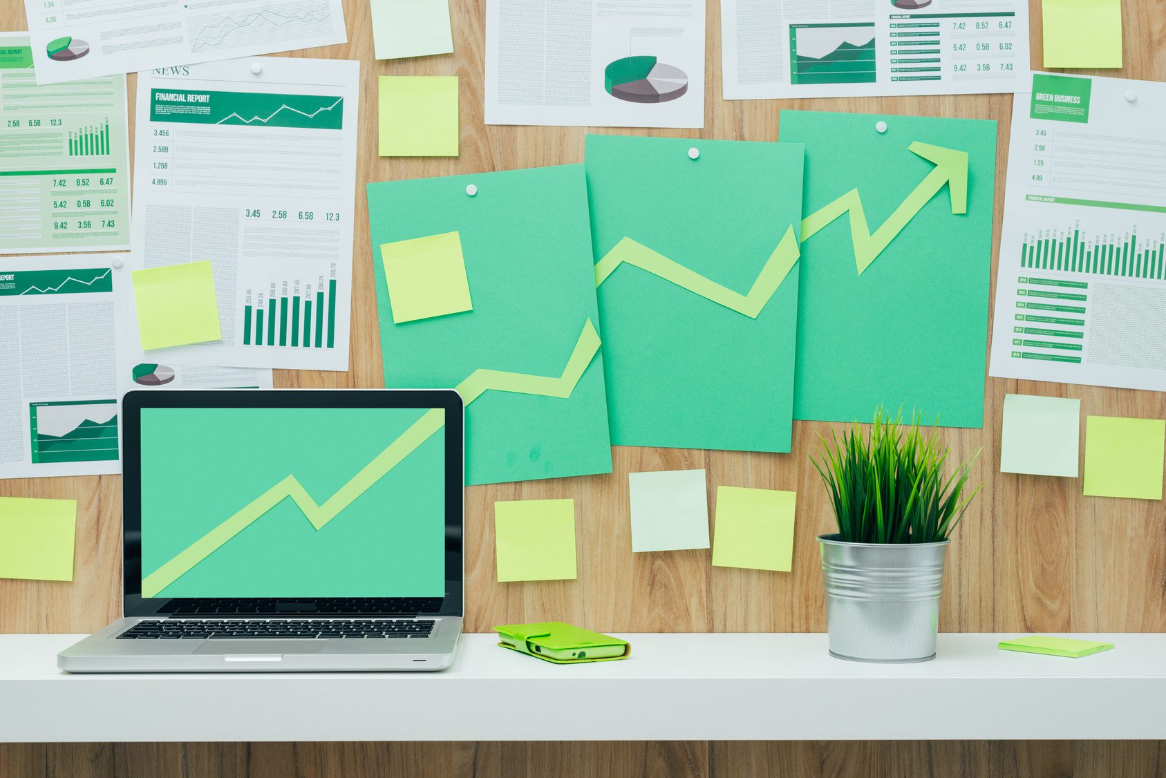 Successful financial chart with arrow pointing up composed of green paper cuts hanging on a wall and laptop, eco business and financial success concept